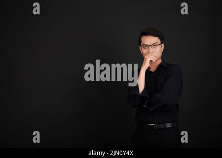 Portrait of pensive serious young man in glasses touching face and looking at camera Stock Photo
