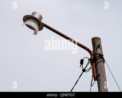 Old rusty destroyed broken street lamp on a rusty metal pole and wooden structure with electric wires Stock Photo