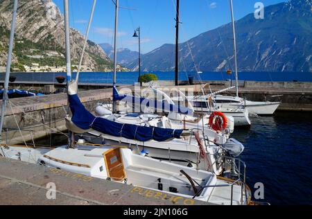 a beautiful old marina in the Italian town of Limone on turquoise lake Garda with mountains in the background (Lombardy) Stock Photo