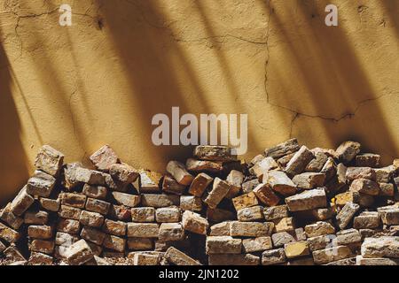 Pile of old bricks stacked in house back yard, leaning on to yellow wall, copy space included Stock Photo
