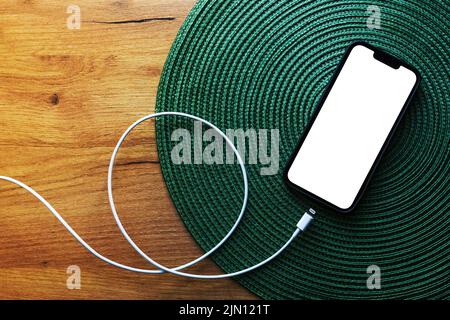 Smartphone with blank mockup screen and mobile charger cable on the table, top view copy space Stock Photo