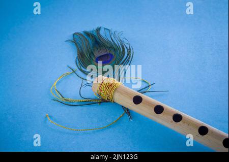 Bamboo flute decorated with peacock feather symbolic to hindu god lord krishna during celebration of janmashtami festival. photo taken in blue backgro Stock Photo