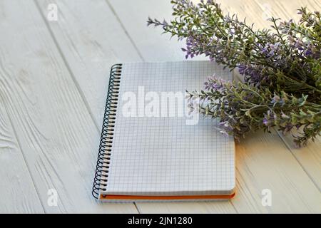 Blank notepad and purple flowers on wooden desk. Checkered page for copy space. Stock Photo