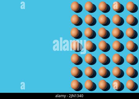 A pattern of brown chicken eggs on the right half of the blue background. Left side for copy space, close-up, top view. Horizontal.
