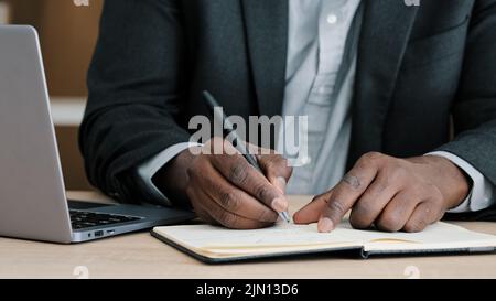 Close-up male hands writing in notebook with pen make notes information financial analysis startup project management idea sitting at desk in office Stock Photo