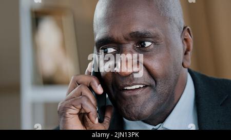 Close-up emotional old 50s wrinkled male face friendly businessman talking phone mobile conversation call answering. Portrait African man boss leader Stock Photo