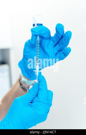 Close-up of the hands of a doctor or nurse with blue surgical gloves preparing a syringe with medicine from a container Stock Photo