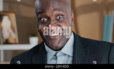 Close up old wrinkled male face surprised amazed African American man makes big eyes feels shock open mouth in astonishment wow reaction joyful happy Stock Photo