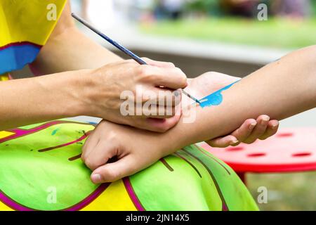 Young girl artist draws drawing on child's hand. Painting skin with paints, close-up, without faces. Stock Photo