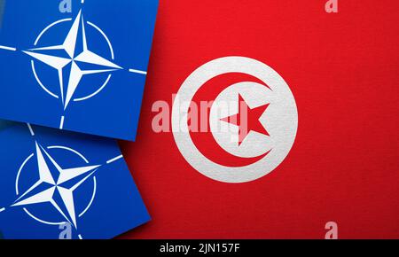 LONDON, UK - August 2022: NATO North Atlantic Treaty Organization military alliance logo on a Tunisia flag Stock Photo