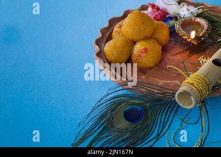 Bamboo flute decorated with peacock feather symbolic to hindu god lord krishna with sweet laddu, diya & flowers during celebration of janmashtami fest Stock Photo