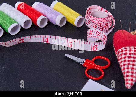 Close up set of sewing accessories on dark surface. Threads with measure tape and scissors. Stock Photo
