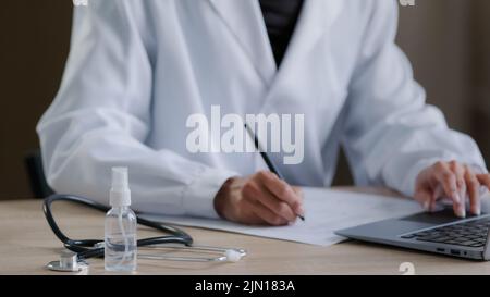 Close up unrecognizable female hand worker doctor practitioner writing prescription noticing documents at desk with medical equipment therapist woman Stock Photo