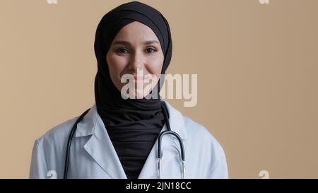 Portrait happy smiling muslim arab woman islamic doctor physician in hijab wear white medical coat looking at camera posing positive young female Stock Photo