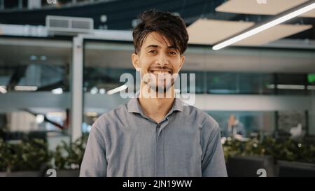 Happy indian bearded handsome adult man stand in hall office smiling looking at camera cheerful male arab brunette guy businessman entrepreneur Stock Photo