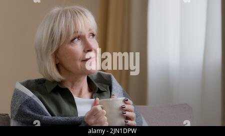 Side view african american old 60s lonely business man drinking coffee tea from cup mug looking out window thinking contemplating daydreaming relaxing Stock Photo