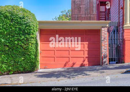 Detached garage exterior with peach wooden garage door at San Francisco, California. There is a shrub wall on the left of the garage and a gate on the Stock Photo