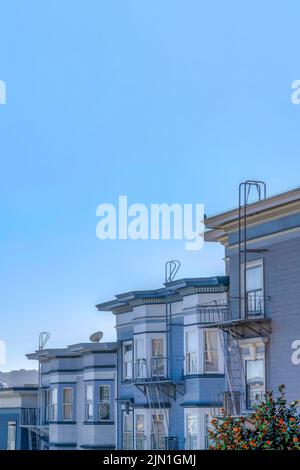 Sloped residential buildings with emergency stairs against the clear sky at San Francisco, CA. Apartment units with gray color schemes and bay windows Stock Photo