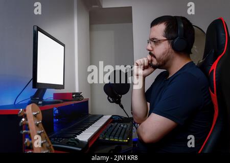 Caucasian Latino music engineer man, with headphones and glasses, is with one hand on his chin and his arms crossed serious and thoughtful, sitting wa Stock Photo