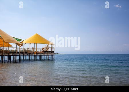Swimming area or pier on the sea. A large pier with a roof, wooden planks and rusty stairs descending into the water. Bathing and resting place. Stock Photo