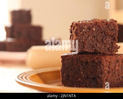 a pile of homemade brownies on a orange dish with a second pile of brownies on the background Stock Photo