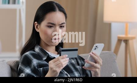 Angry puzzled Asian woman try to pay with e-bank app online service has problem with credit card blocked financial limit not activated for internet Stock Photo
