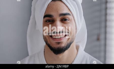 Closeup male face with acne headshot portrait smiling toothy handsome arabian indian bearded man with bath towel on head standing in bathroom. Healthy Stock Photo