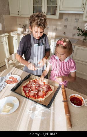 Children cook pizza together at home in the kitchen. Stock Photo