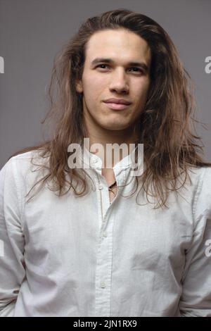 Handsome calm man. Portrait of a young muscular guy with long hair. Strong boy on an isolated grey background in the studio Stock Photo