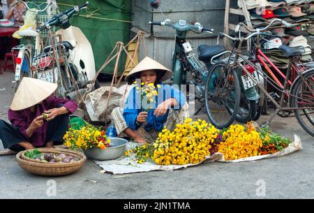 Vietnamese woman selling flowers in a Hanoi market, wearing traditional conical hat, Vietnam Stock Photo