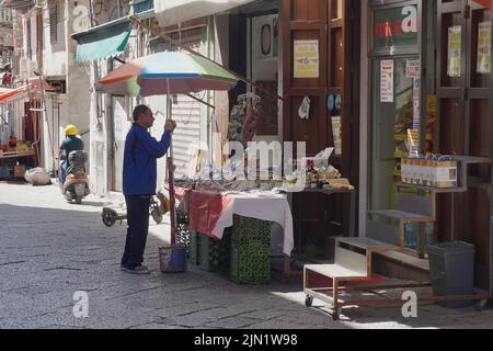 A shopkeeper in a street market in Palermo, Sicily, prepares a stall outside his shop Stock Photo