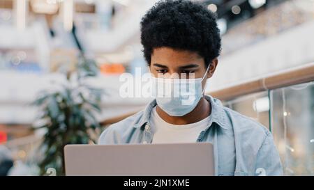 Portrait african american guy student user business man in medical mask thinking plan creates idea strategy working with laptop thoughtful pondering Stock Photo
