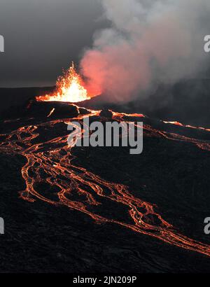 A dramatic night view of an erupting volcano with flowing lava and ...
