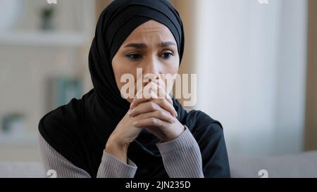 Upset sad girl in hijab sit alone get bad news feel depressed frustrated muslim woman suffering from illness worried about unresolved problems feeling Stock Photo