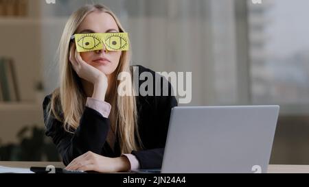 Lazy funny sleeping girl caucasian business woman tired sleepy female worker with sticky notes on eyes glasses with stickers sleeps in office feeling Stock Photo