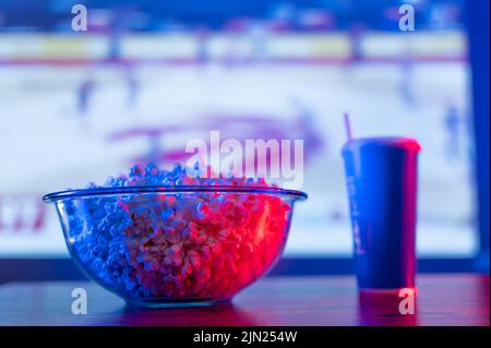 A sports match on the big TV screen. Large glass bowl with popcorn, carbonated drink in a plastic glass. Relax in front of the TV, watch your favorite Stock Photo