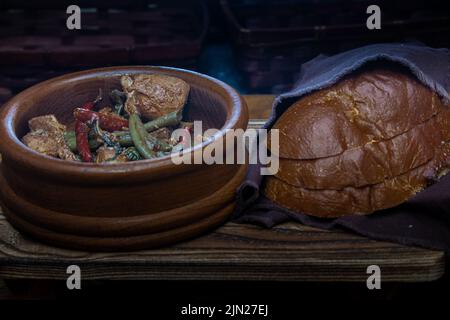 Adobo chicken with peppers in wooden bowl with sliced sourdough bread. Stock Photo