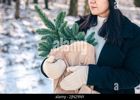 A woman holds a craft bag with Christmas tree branches in the winter forest. Stock Photo