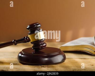Close-up. Wooden judge's gavel and an open book on a beige background. Court and justice, Constitution, Bible, rule of law. There are no people in the Stock Photo