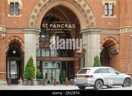 London, Great Britain - July 3, 2022: Closeup of central entrance on red brick historic St. Pancras Renaissance Hotel facade with silver car up front. Stock Photo