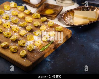 Homemade raw dumplings on a wooden cutting board. ravioli. as well as ingredients, kitchen utensils on a dark blue background. Meat dumplings. ravioli Stock Photo