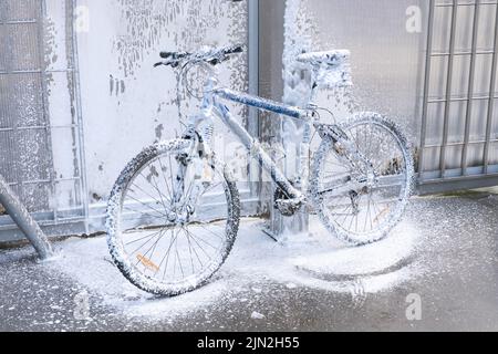 Washing a bicycle with a foam jet at a car wash. The bike is covered with foam. Self-service. Bicycle maintenance. Stock Photo