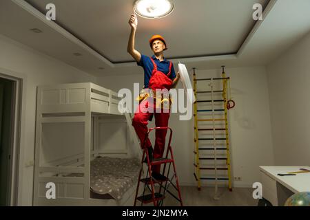young man repairing cable wiring and installs or replaces the halogen lamp on the ceiling. Stock Photo