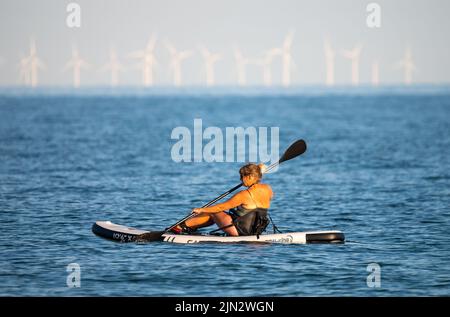 Littlehampton, West Sussex, UK. Monday 8th August 2022. A lady paddles out at sea late this evening as the heatwave continues on the south coast. Credit: Geoff Smith/Alamy Live News