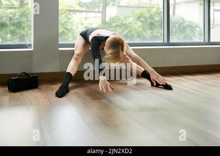 Female dancer bending forward to stretch legs before intense training Stock Photo