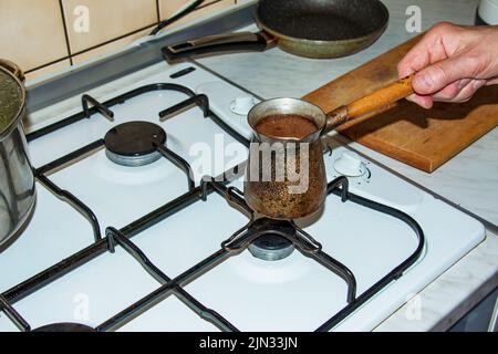 Ground coffee is brewed in a copper cezve on a gas stove. Stock Photo