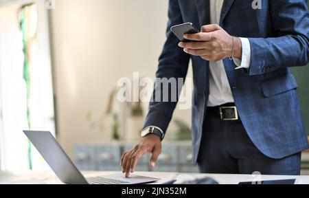 Business man wearing suit holding phone using laptop online technology. Stock Photo