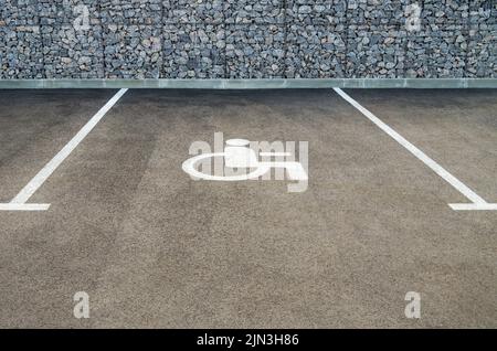Parking space for people with disabilities marked with white paint on the asphalt in front stone wall Stock Photo