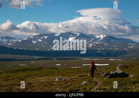 A hiker with a huge backpack on a trail between the Swedish Blahammaren and Norwegian Storerikvollen Mountain stations, Jamtland, Sweden Stock Photo