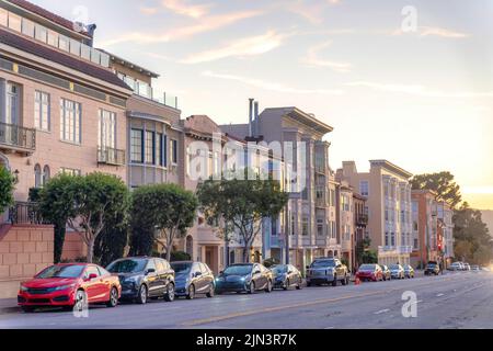 Road with parked vehicles at the front of residential buildings in San Francisco, CA. There are large houses and apartments in a row near the street w Stock Photo